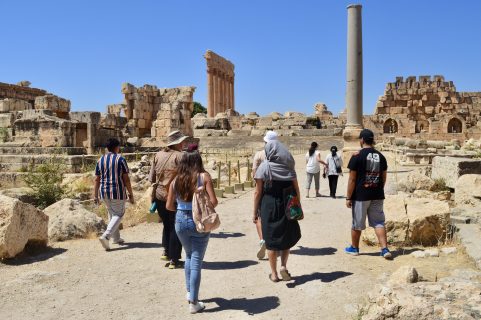 A view of an archaeological site with visitors in the foreground, ruins of a building in the background.