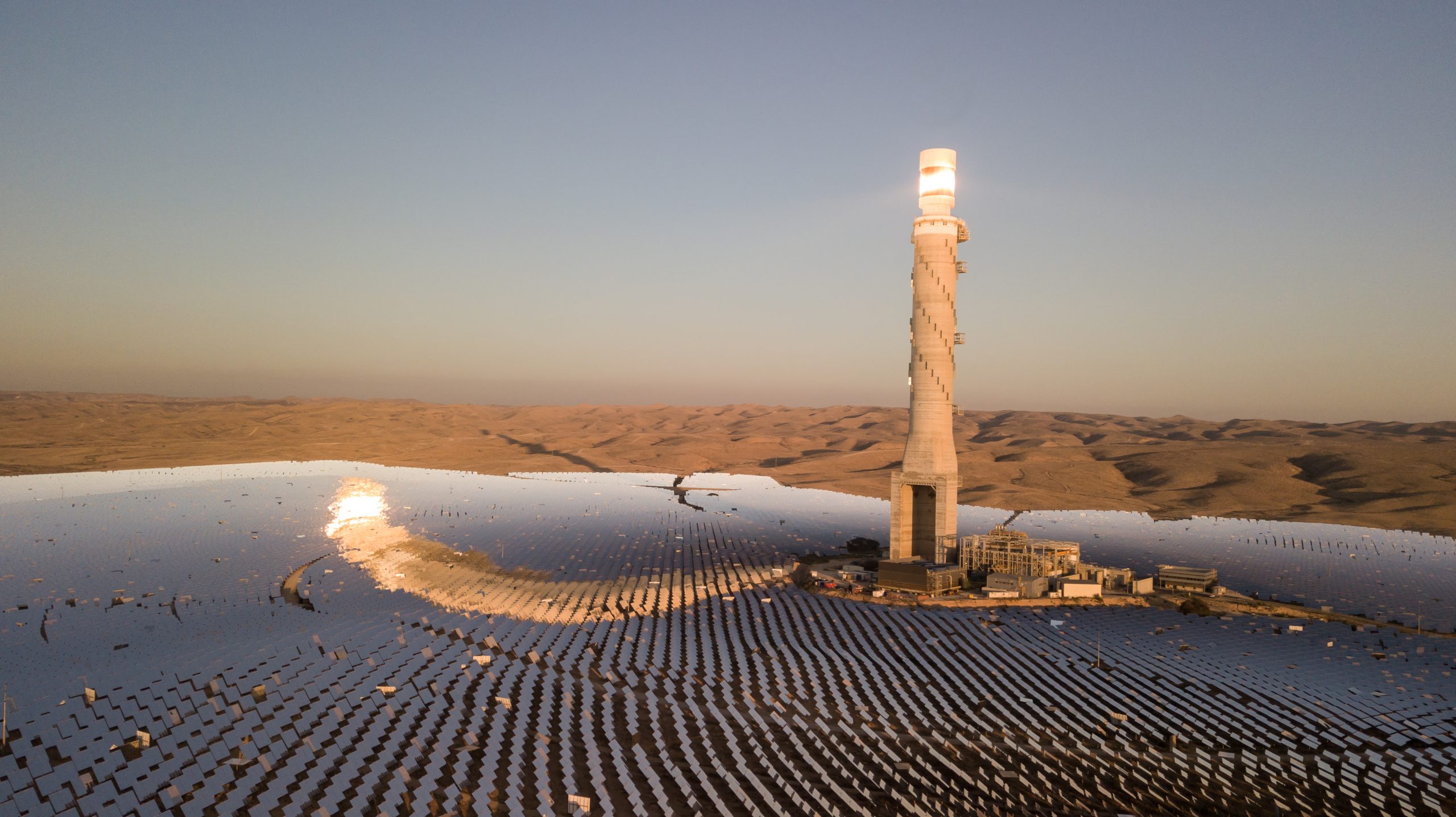 View of desert landscape with hundreds of solar panels surrounding a lighthouse-looking tower.