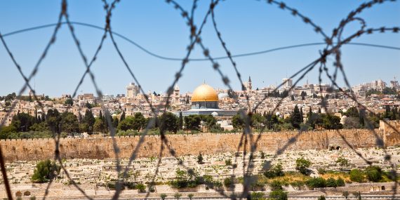 Kuvassa näkyy piikkilanka-aidan välistä Jerusalemin vanha kaupunki ja sen kultakupolinen moskeija.