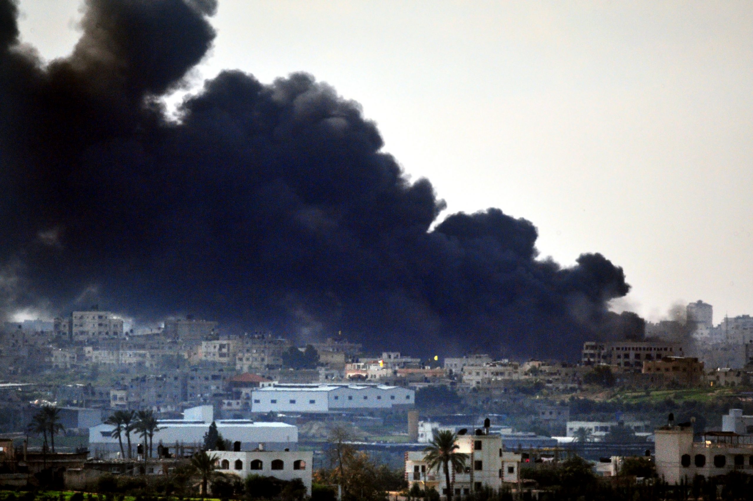 Kuvassa kerrostaloja Gazassa pommituksen jälkeen- Talojen taustalla ilmaan kohoaa paksu, tumma savupilvi.