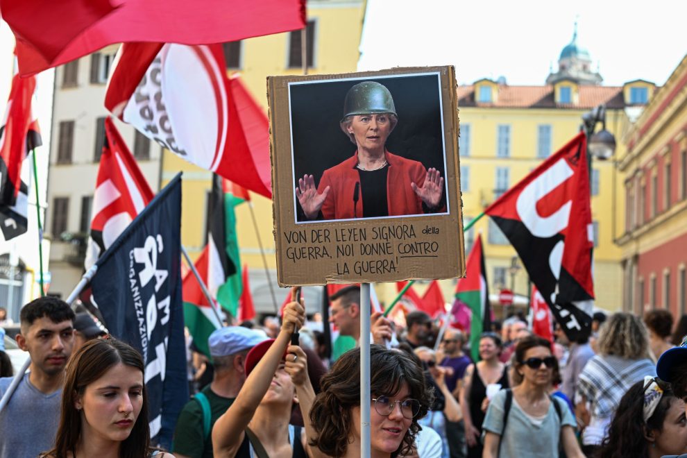 Artikkelikuva: Mielenosoitus Milanossa 20.6.2025. Mielenosoittajan kyltissä on kuva Euroopan komission puheenjohtaja Ursula von der Leyenistä sotakypärä päässä. Kyltissä lukee: Von der Leyen on sotarouva, me taas olemme sotaa vastustavia naisia.