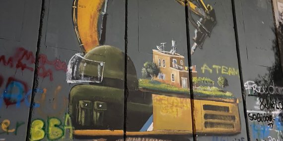 Graffiti keltaisesta paalutuskoneesta, jonka ohjaamo on kuvattu sotilaan kypäränä. Koneen selässä on ruksea, tasakattoinen asuintalo puutarhoineen, mitä koneen käsivarsi uhkaa.