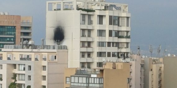 Beirutin kaupunkimaisema, jossa vaalea kerrostalo etualalla; rakennuksen julkisivussa näkyy suuri musta nokijälki usean kerroksen korkeudella. Ympärillä on muita asuinrakennuksia ja taustalla pilvinen taivas.