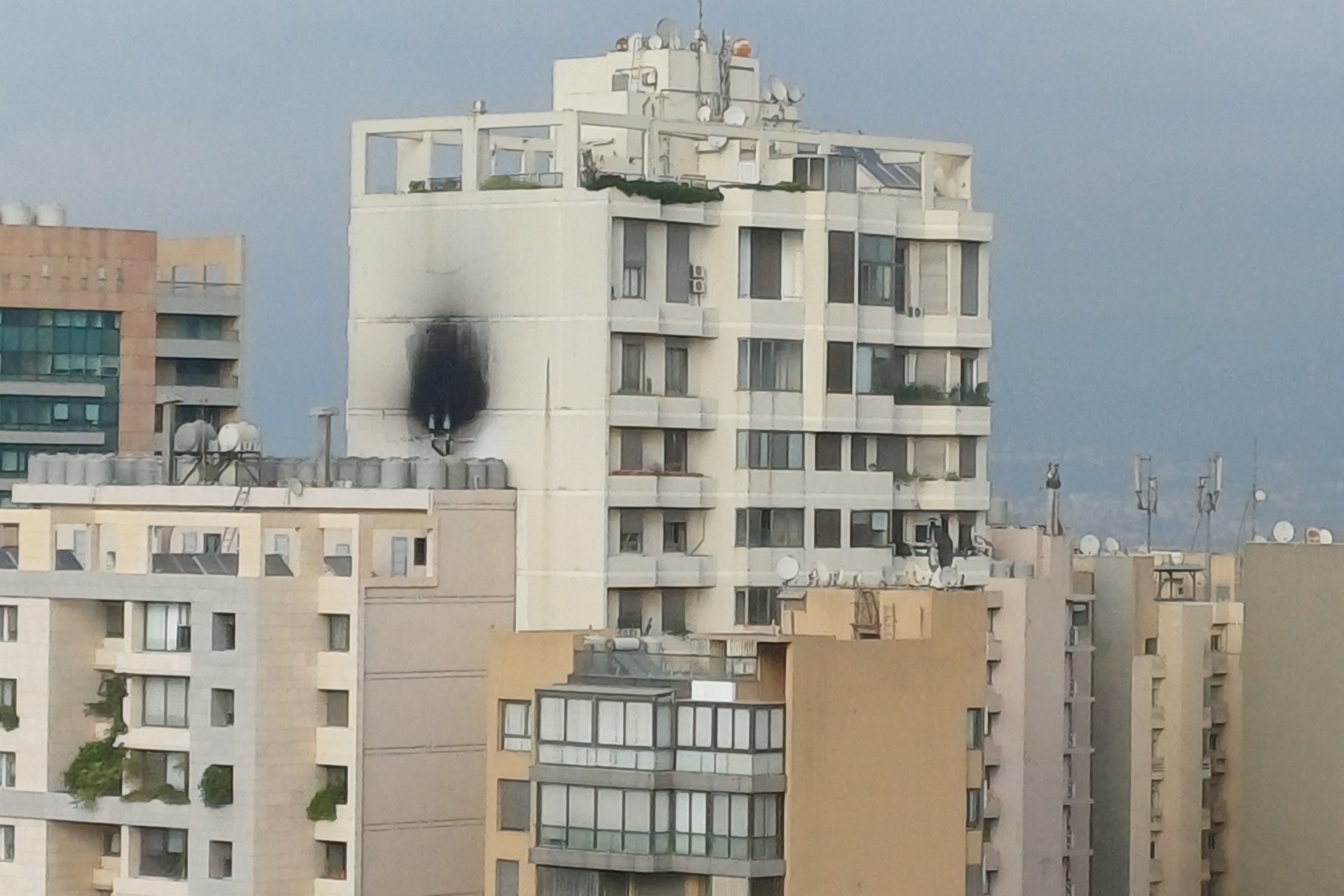 Beirutin kaupunkimaisema, jossa vaalea kerrostalo etualalla; rakennuksen julkisivussa näkyy suuri musta nokijälki usean kerroksen korkeudella. Ympärillä on muita asuinrakennuksia ja taustalla pilvinen taivas.