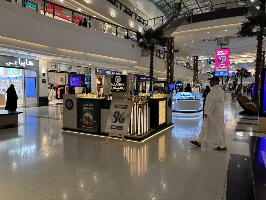 Hajuvesien myyntikoju ja sen ohi kävelevä mies Gallery Mall -kauppakeskuksen aulassa Riadissa. Myyntikojun edustalla tarjouskyltti, joka mainostaa 96 rialin tarjoushintaisia tuotteita. 