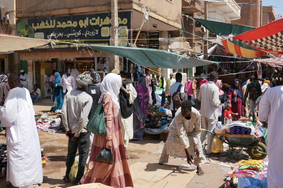 Khartoumin vilkas katumarkkina Sudanissa. Ihmisiä kulkee ja asioi kojuilla, joissa myydään muun muassa vaatteita ja muita tavaroita. Katua reunustavat kauppaliikkeet ja myyntikojut, joita varjostavat värikkäät markiisit.